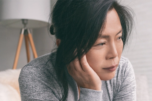 Adrenal-Fatigue-Doctor A middle-aged asian woman sitting on her couch, resting her head on her hand, suffering from adrenal fatigue. Get treatment for adrenal fatigue syndrome from Proactive Wellness Centers in Loudoun County.
