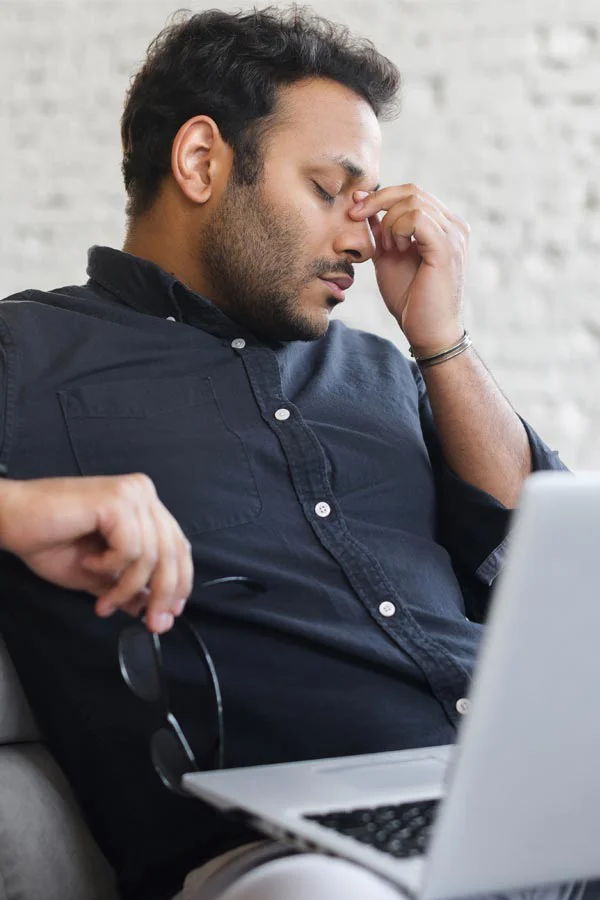Adrenal-Fatigue-Treatment A middle-aged man with a laptop closing his eyes and rubbing his nose. He needs treatment for Adrenal Fatigue Syndrome from Proactive Wellness Centers in Loudoun County.