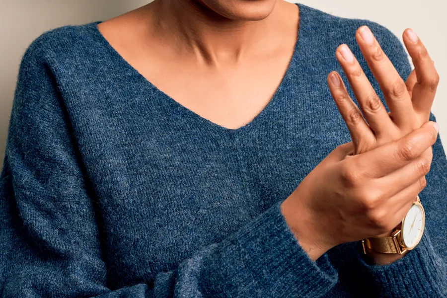 Arthritis-Doctor Close up of a woman in a blue sweater massaging one aching hand with the other. Get help for arthritis from Proactive Wellness Centers in Loudoun County.