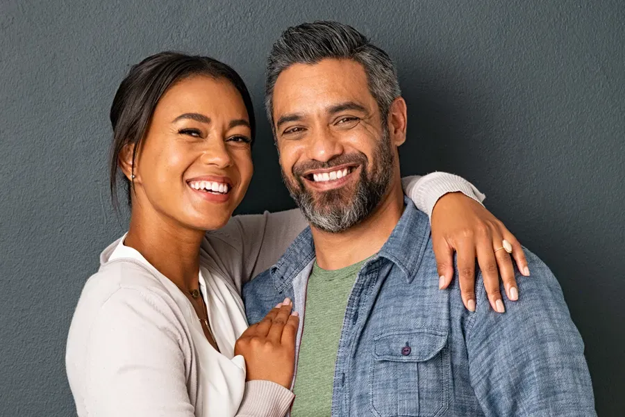 Bioidentical-Hormone-Therapy-Doctor A middle-aged couple with their arms around each other standing against a gray background and smiling, happy with the bioidentical hormone therapy they received from Proactive Wellness Centers in Loudoun County.