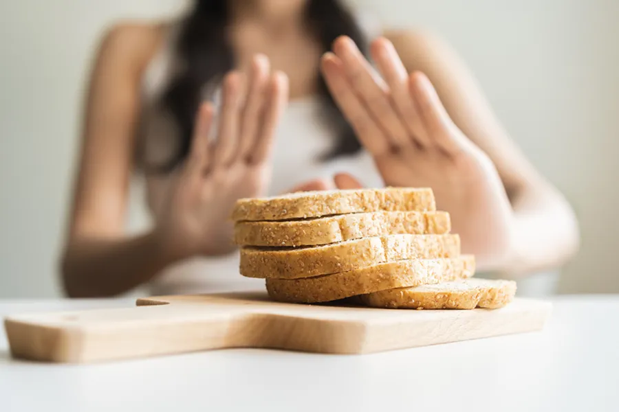 Celiac-Disease-Clinic Close up of a stack of bread slices on a cutting board with a woman's hands behind them, refusing to eat. Get treatment for Celiac Disease from Proactive Wellness Centers in Loudoun County.
