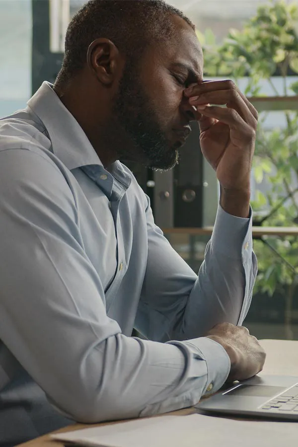 Chronic-Fatigue-Treatment A black man rubbing the top of his nose at his desk, in need of chronic fatigue treatment from Proactive Wellness Centers in Loudoun County.