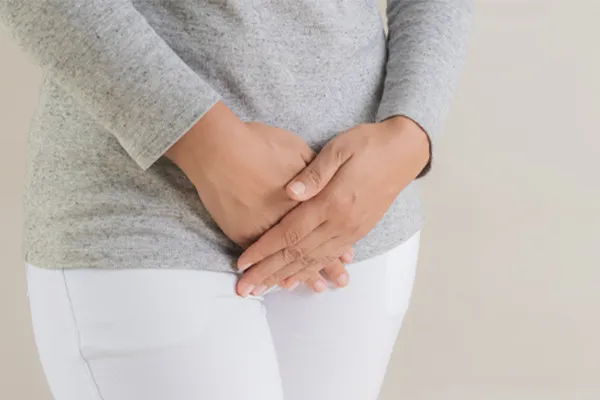 Fibroids-Clinic Close up of a woman in a gray shirt and white pants holding her hands below her abdomen in discomfort. Get treatment for fibroids from Proactive Wellness Centers in Loudoun County.