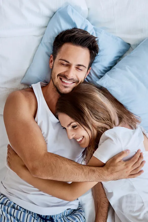 Gainswave-Treatment A couple in pajamas embraces laughing in their bed. Get Gainswave treatment from Proactive Wellness Centers in Loudoun County.