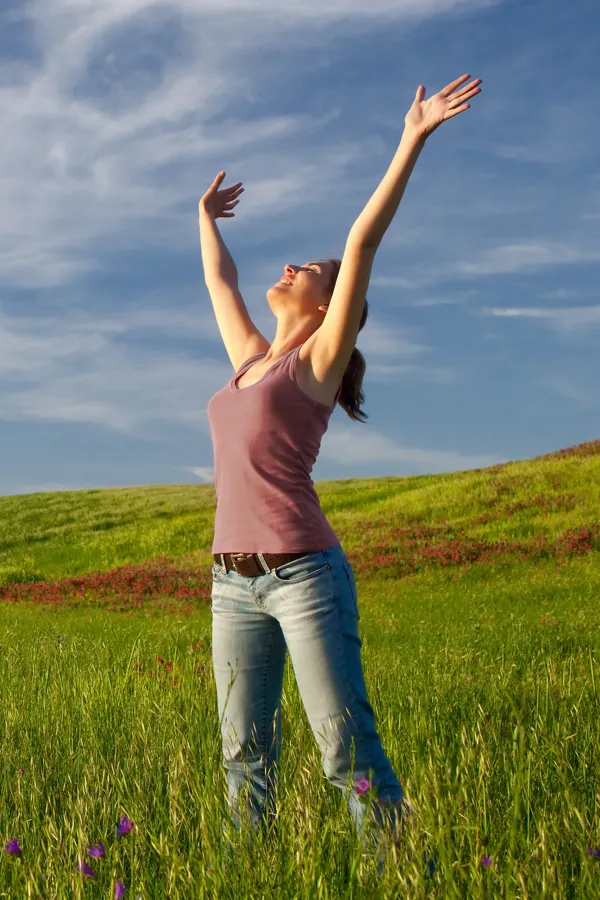 Graves-Disease-Treatment A woman in a tank top and jeans looks up with her arms outstretched to the sky in a field after successful treatment for Grave's Disease from Proactive Wellness Centers in Loudoun County.