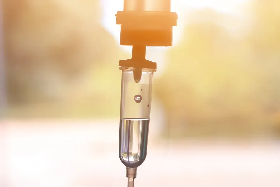 IV-Therapy-Doctor Close-up of an IV drip warmly lit by a window showing trees and a sunset, representing IV therapy from Proactive Wellness Centers in Loudoun County.