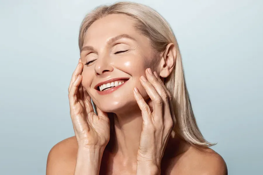 PRP-Facelift-Facial-Doctor A beautiful mature blonde woman touches her face, happy with her PRP facelift and facial injections from Proactive Wellness Centers in Loudoun County.