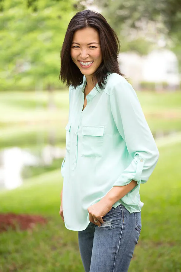 Perimenopause-Treatment A middle-aged brunette woman in a light green button-up shirt stands outside smiling, happy with her perimenopause treatment from Proactive Wellness Centers in Loudoun County.