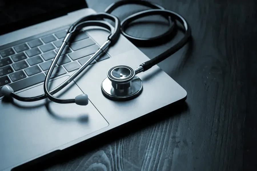 Telemedicine-Doctor An open laptop with a stethoscope lying on it on a wooden table, symbolizing telemedicine care from Proactive Wellness Centers in Loudoun County.