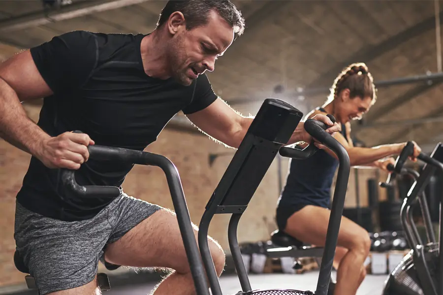 Tirzepatide-Doctor A couple in a brick gym work as hard as they can on exercise bikes, inspired by successful Tirzepatide treatment from Proactive Wellness Centers in Loudoun County.