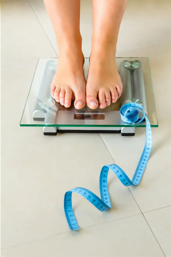 Weight-Loss-Resistance-Treatment Close-up of a woman's feet standing on a scale, with measuring tape by her toes, getting treatment for weight loss resistance from Proactive Wellness Centers in Loudoun County.